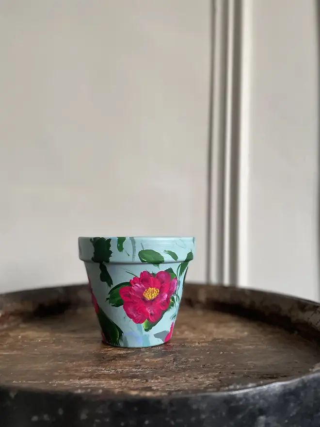 hand painted terrecotta floral plant pot background in a pale blue with rich pink camellia flowers