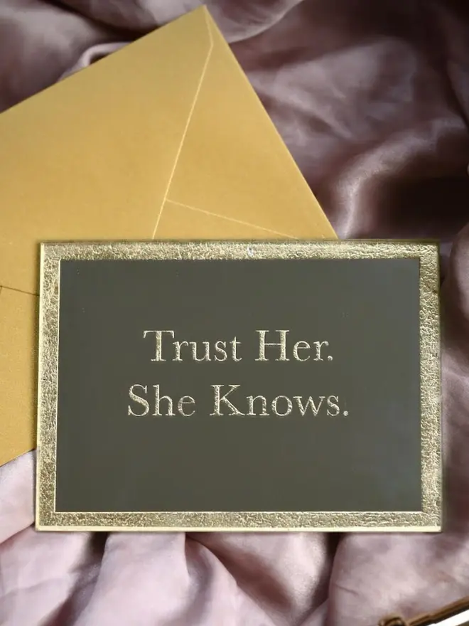 'Trust Her. She Knows' gold etched mirror on pink silk backdrop with gold envelope
