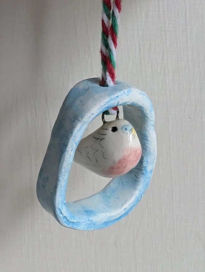 tiny ceramic pink budgie bird hanging in a blue ceramic hoop