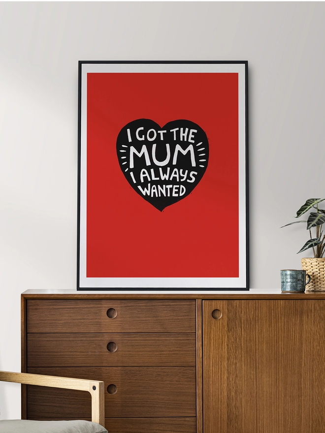 a framed red Woodism linocut digital print sitting on a sideboard. The print reads: 'I Got The Mum I Always Wanted' 