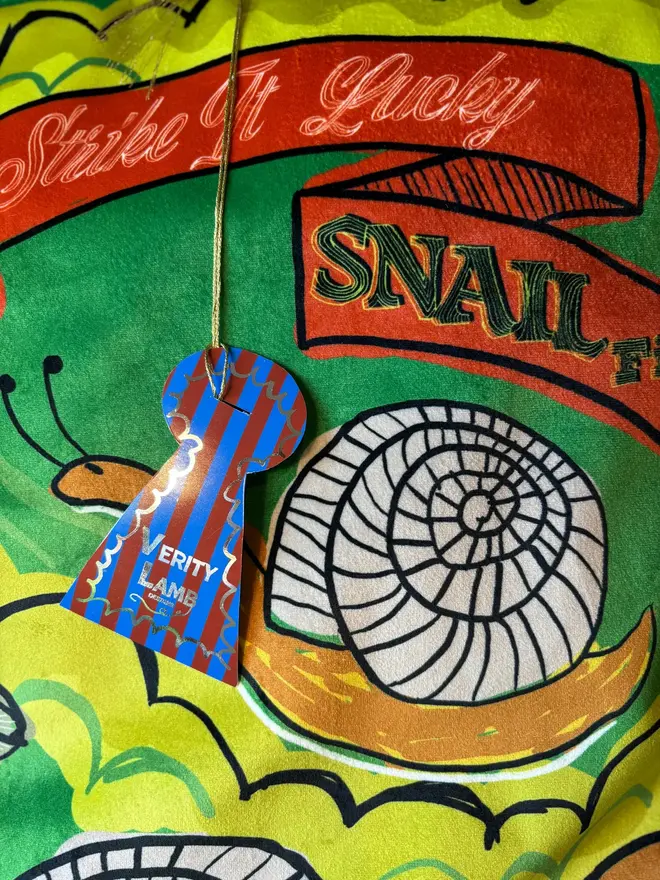 Snail Matchbox Cushion, a green decorated cushion sitting on a decorated surface. 