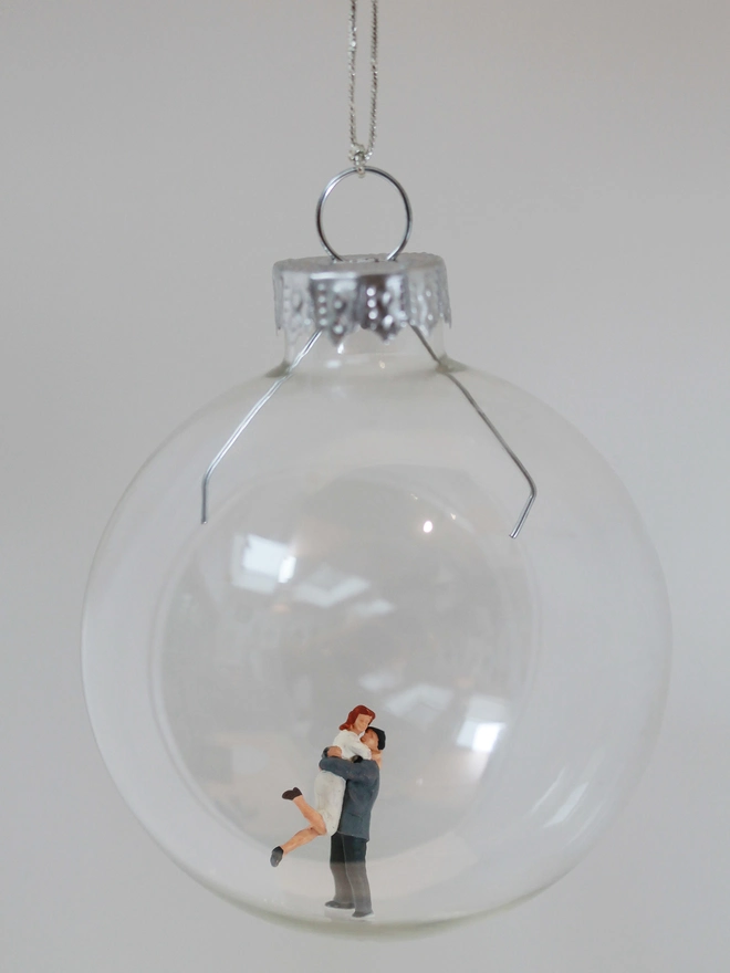 Miniature figure of couple hugging in a glass Christmas bauble