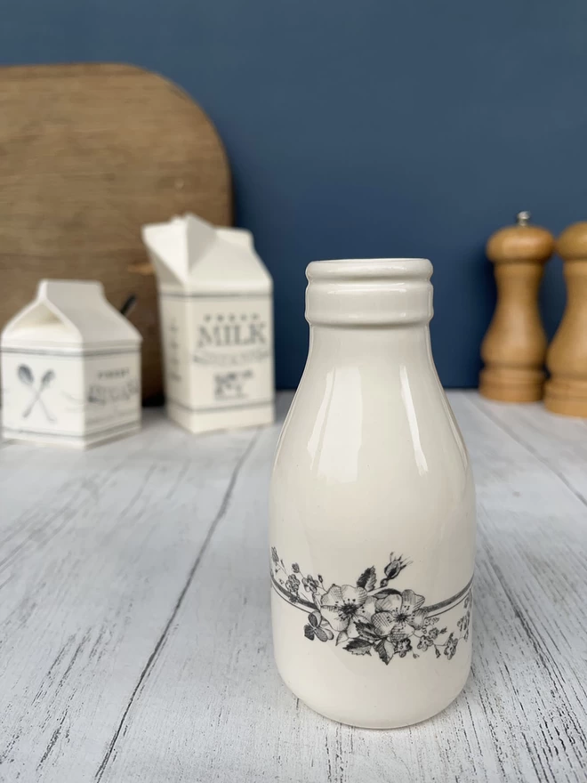 A small handmade ceramic ‘milk’ bottle/vase is decorated with spray of wild flowers.