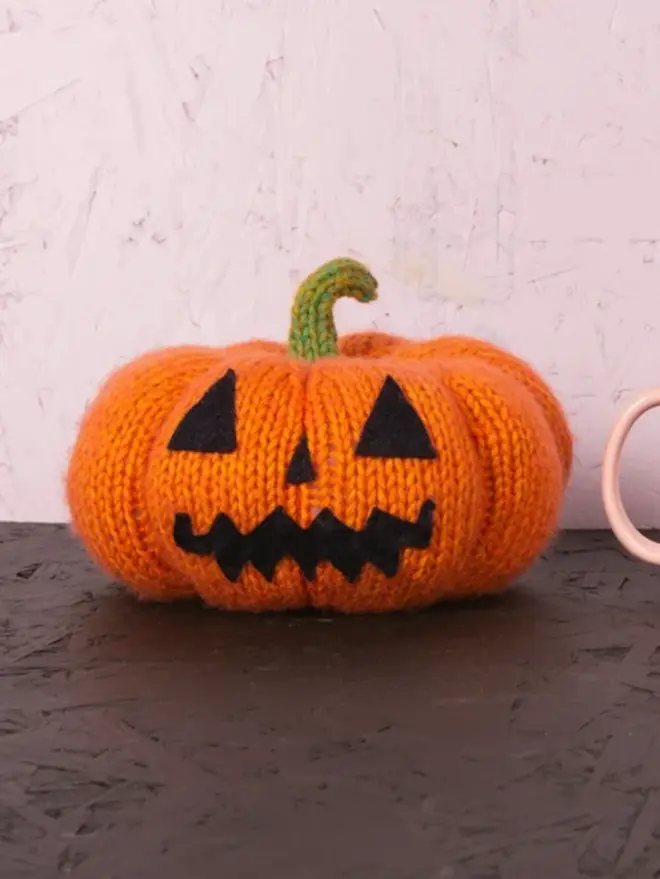 knitted pumpkin, with jack o lantern faces on stone table