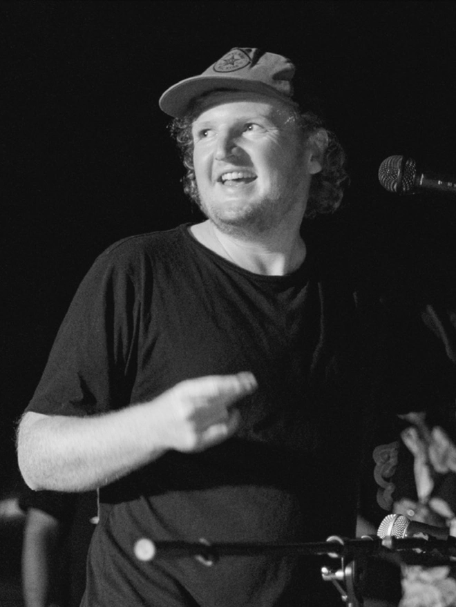 Man standing in front of microphone, smiling and clicking fingers