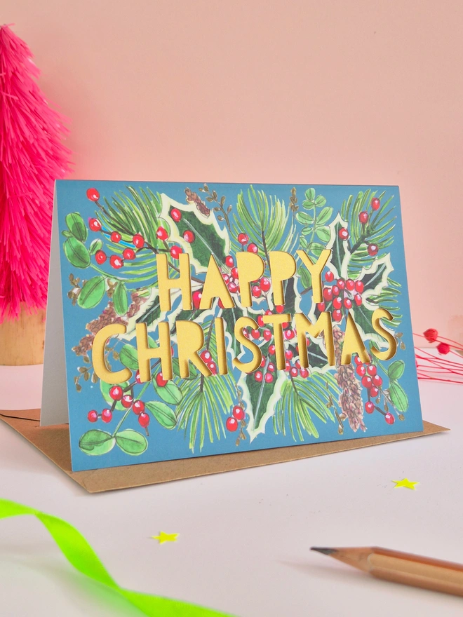 Holly illustration Christmas card with paper cut text and pearlescent gold backing paper 