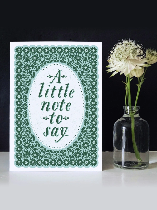 green floral note card with a little note to say on dark background with white flower