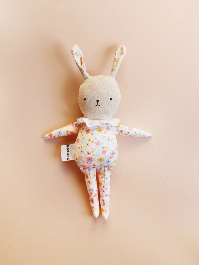 natural linen rabbit doll with printed floral outfit and ruffled white lace collar with embroidered gentle face feature.