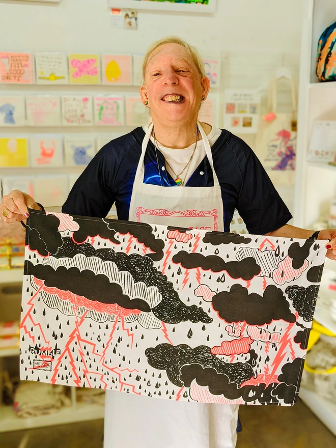 Happy artist holding rumble 100% organic cotton charity tea towel featuring clouds & lightening 