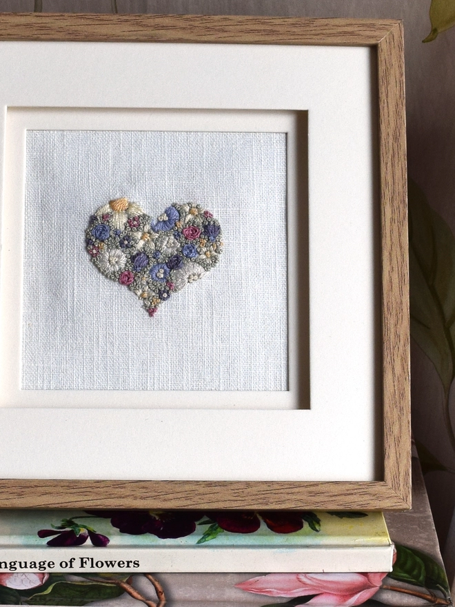 An embroidered Heart, of Lavender Blues and Buttermilk yellow blossoms.  Displayed in a wooden Oak effect Frame with the glass removed. 