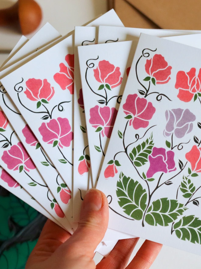 Cottage garden sweet pea flower notecard held in hand showing A6 size (105 x 149mm). Hand-carved botanical greeting card from set of 8, linocut print on recycled cardstock. Eco-friendly stationery with kraft envelope.