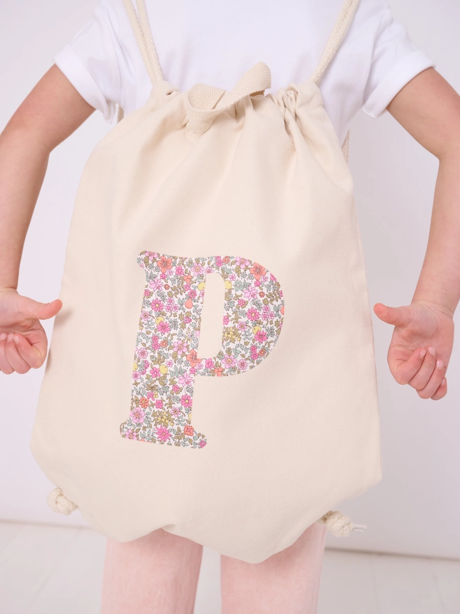a 5 year old girl wearing a Magnificent Stanley Personalised Liberty Print Drawstring Backpack with her initial on in floral print