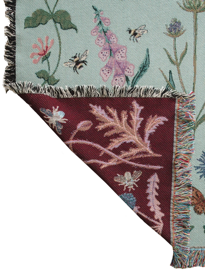 'Pollination Meadow' Recycled Cotton Blanket seen with the corner folded up showing the red blanket.