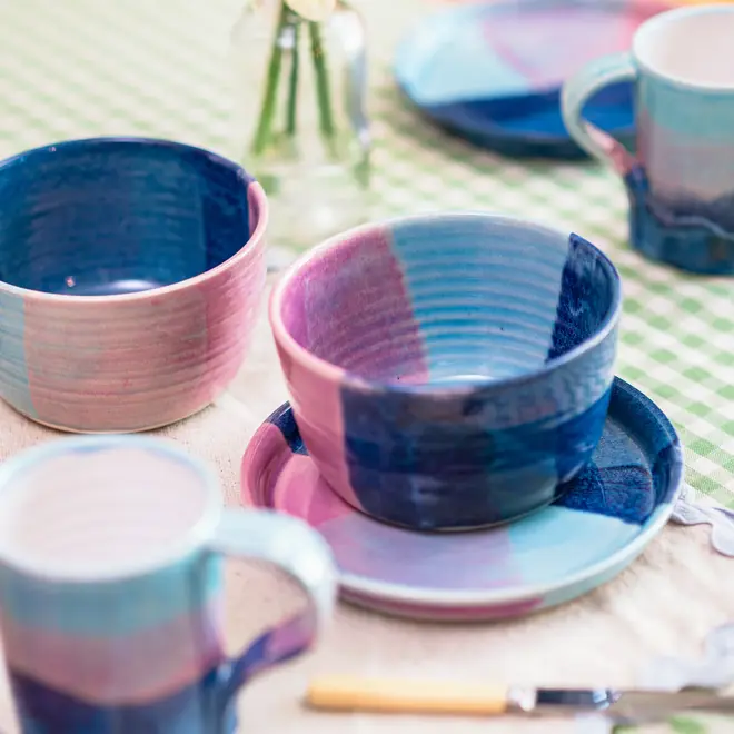 Landscape Breakfast (Set Of 2), a collection of colourful breakfast ceramics placed on a table. They are accompanied by a green table cloth and some flowers. 