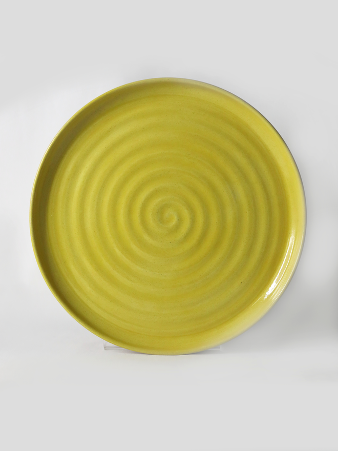 A handmade ceramic side plate in sun yellow glaze, photographed from the front against a plain white background, showing a natural concentric swirl texture from the wheel-throwing process