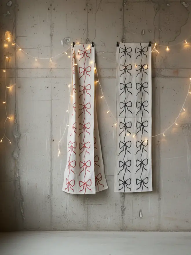 Hand Painted Bow Print Sustainable Linen Table Runner, a pair of table runners hanging against a wooden background. 