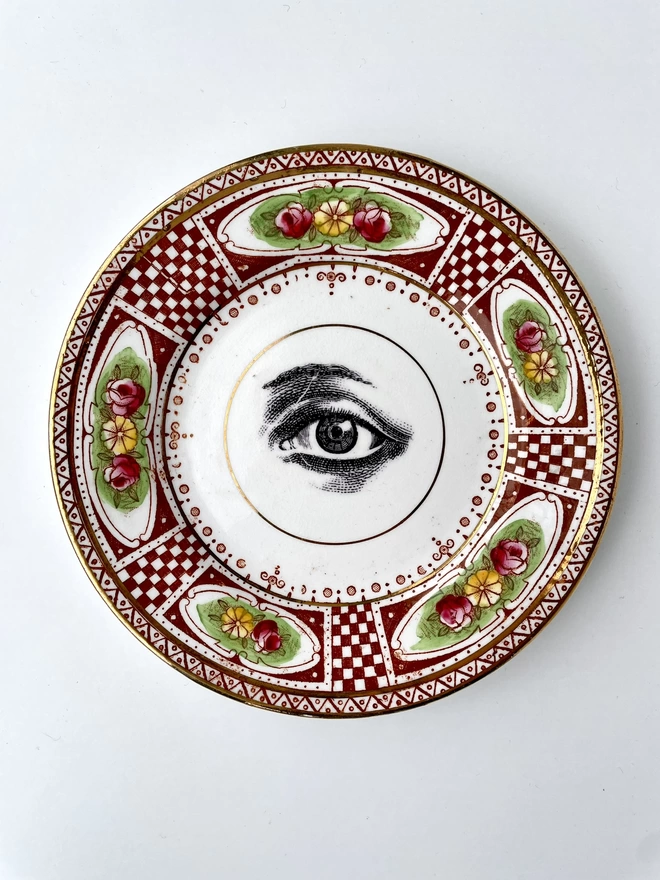 vintage plate with an ornate border, with a printed vintage illustration of an eye in the middle 