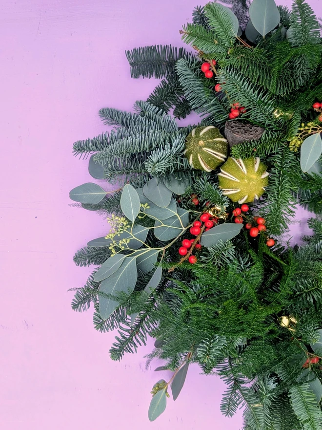 Fresh handmade Christmas wreath with fir, eucalyptus, red berries, dried citrus, and natural seed pods, finished with a red velvet ribbon edged in gold traditional festive front door decoration