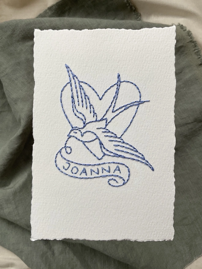 Swallow with banner design hand stitched in blue thread on white khadi paper