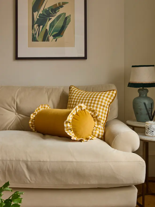 Mustard gingham Striped Bolster cushion with ruffles on a cream sofa in a living room setting