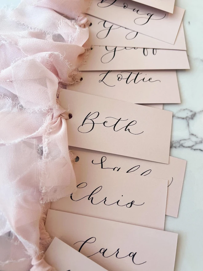 Personalised Calligraphy Wedding Pink Place Cards, pink wedding cards with pink ribbons grouped together. 