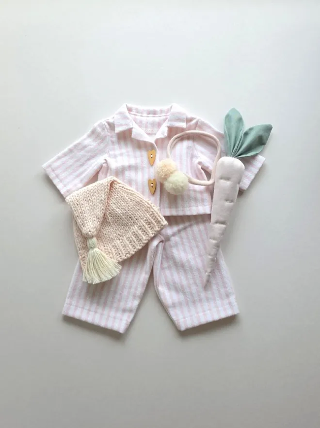 Flat lay pink striped Christmas Eve bunny pyjamas with knitted sleepy hat, alpaca pom-pom headband and handmade reindeer carrot.