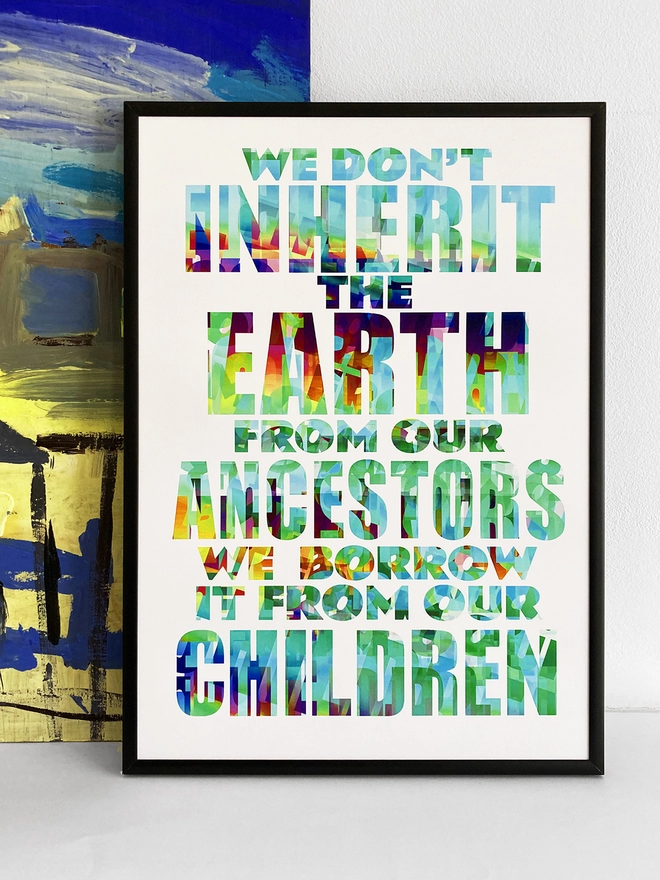 Framed multicoloured typographic print of a Pulp song lyric from Common People - “We don't inherit the earth from our ancestors, we borrow it from our children”.  The print rests against a blue and yellow abstract painting.