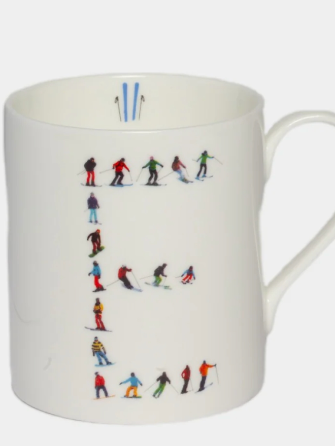 A simple white mug illustrated with an ‘E’ made of small, multicoloured skiers. The mug is set against a plain, white background.