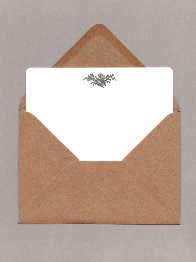 White notecard with black flowers at the top inside an open kraft envelope