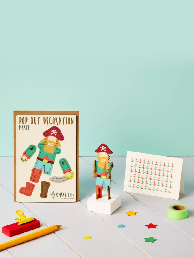 3D pirate decoration and anchor pattern greeting card and brown kraft envelope on top of a grey desk in front of a light green coloured background