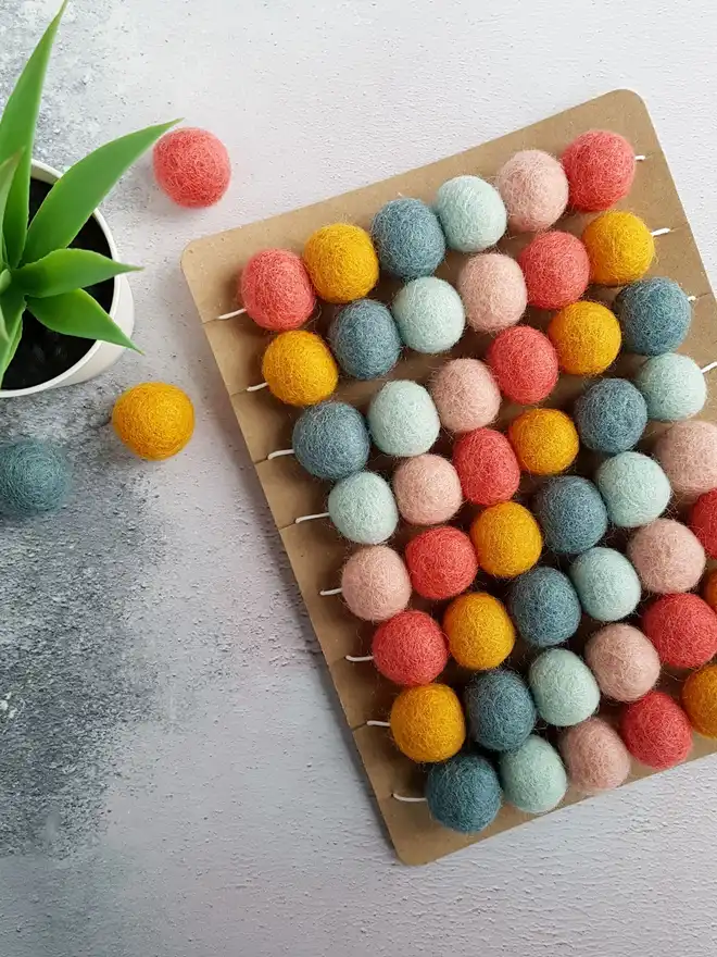 A pastel felt ball garland wrapped around a display card.