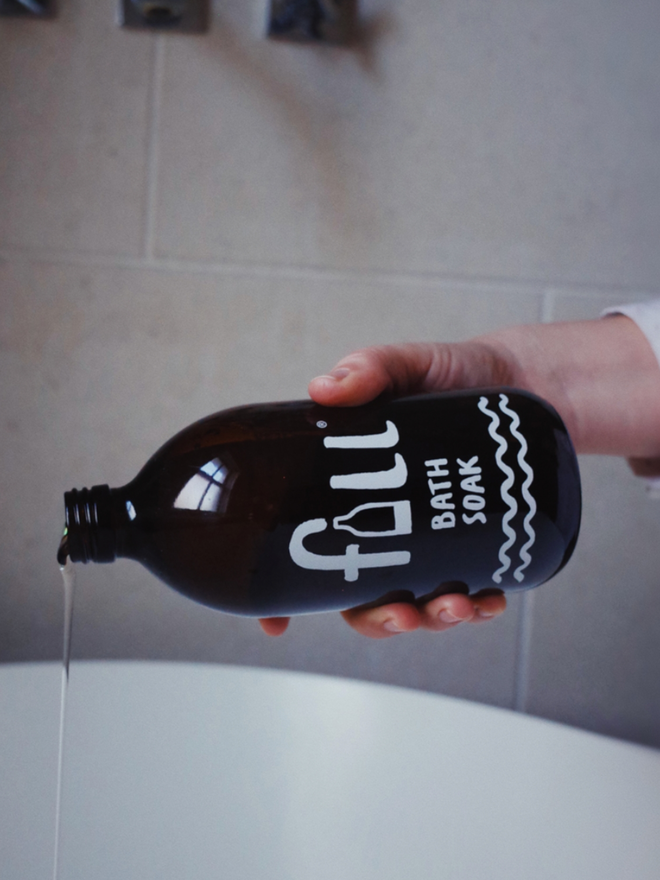 Bath Soak. An amber glass bottle reading Fill Bath Soak being poured into a bath.