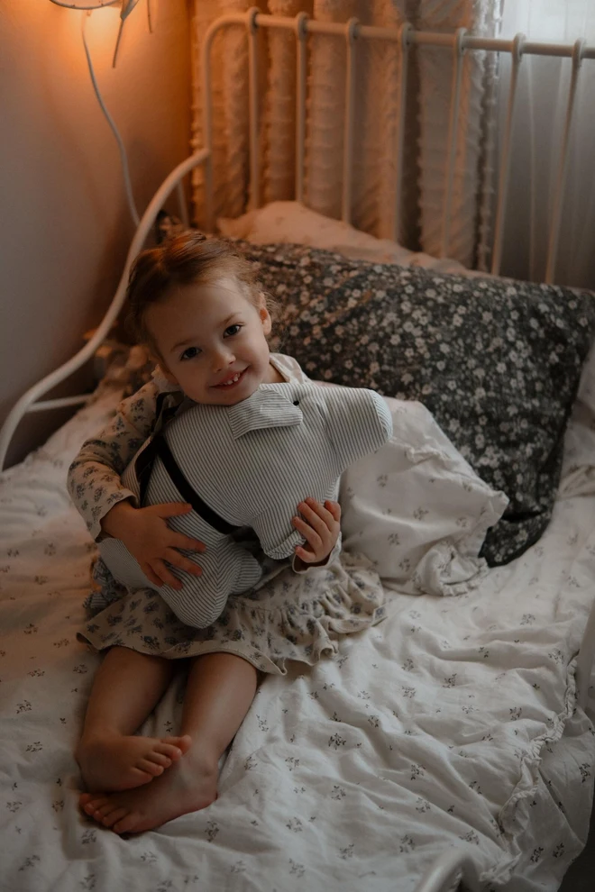 Cotton Pig Plushie, a child with their pig plushie sitting on their bed. 