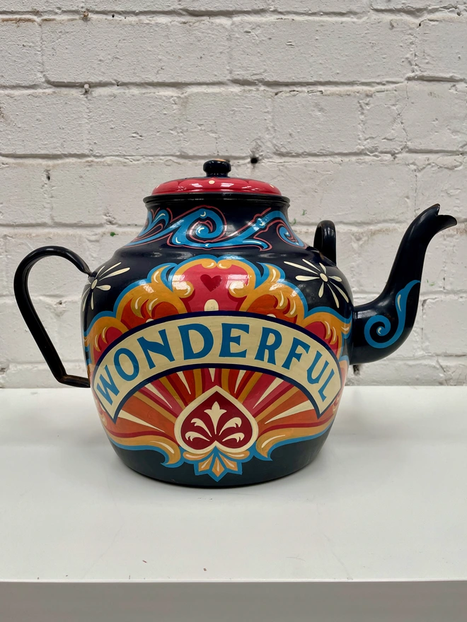 Large dark blue vintage enamel teapot, hand-painted with a oink, orange a yellow fairground inspired design. 'Wonderful' is painted in a banner across the centre of the design.