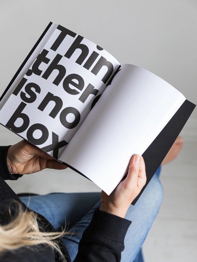 Lady holding open a Hello Notes A5 Notebook on a quote page reading 'Think there is no box'