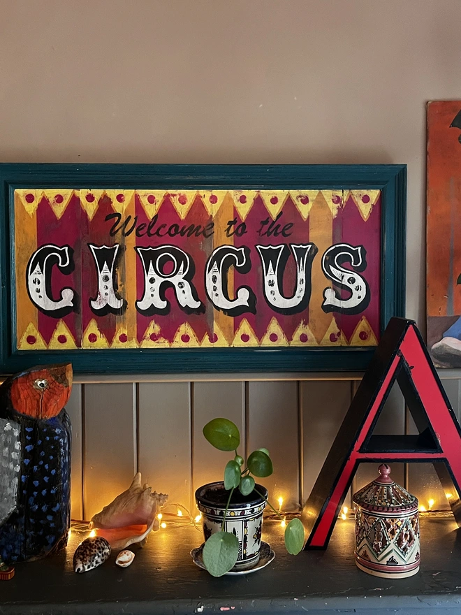 welcome to the circus sign, with colourful stripes of pink, yellow and orange with a teal frame and zig zag pattern at the top and the bottom. surrounded by a teal frame