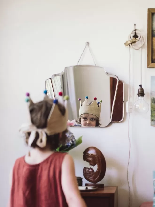 Child wearing the Old Gold Pom Pom Crown looking in a mirror.