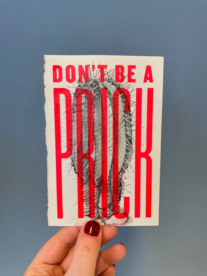 Hand holding a hand pulled screen print over a vintage book page of a cactus with the words ' don't be a prick' over the top in flouro red ink