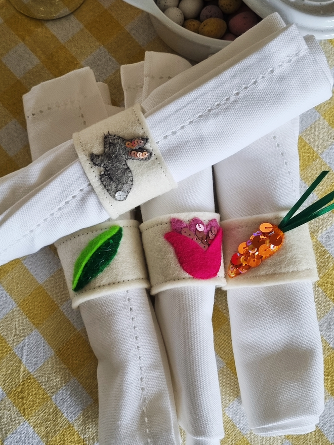 the spring set of napkin rings around white napkins. The bunny, peapod, tulip and carrot pictured