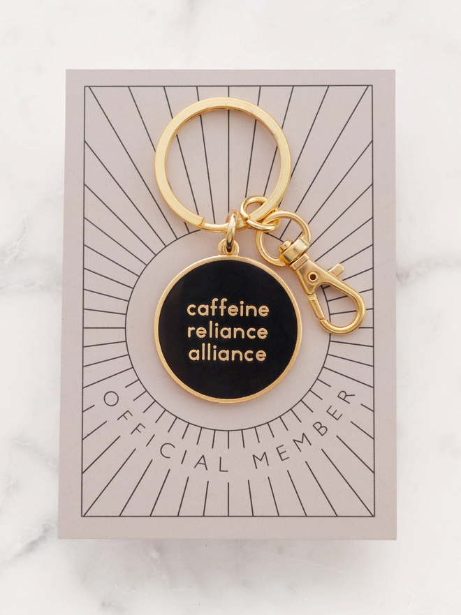 Caffeine reliance alliance enamel keyring on 'official member' backing board