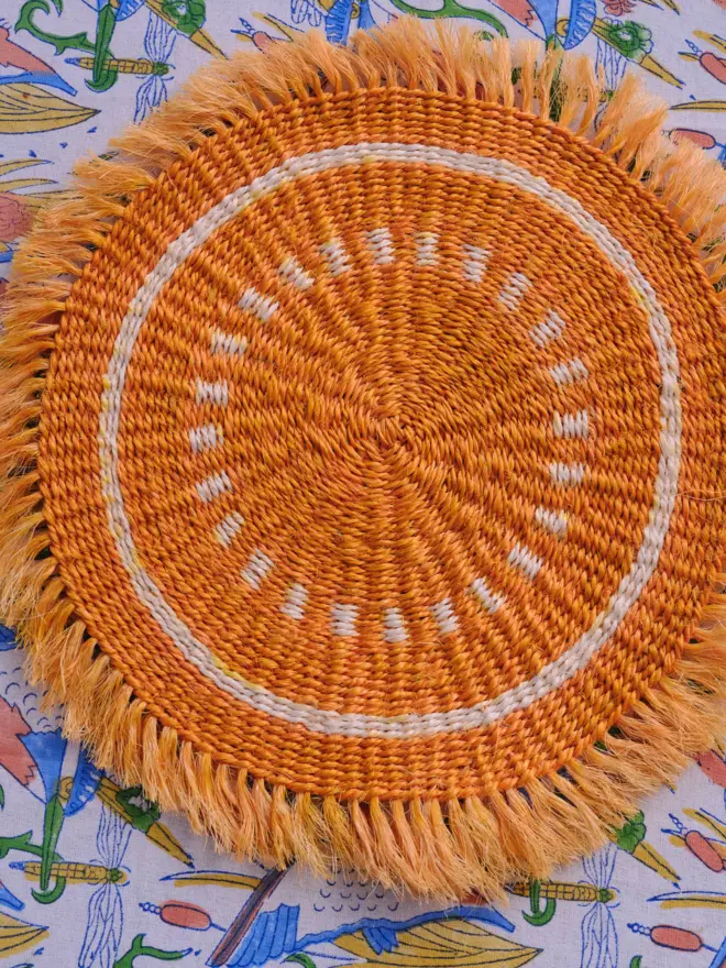 A yellow fringed placemat sitting on top of a colourful tablecloth