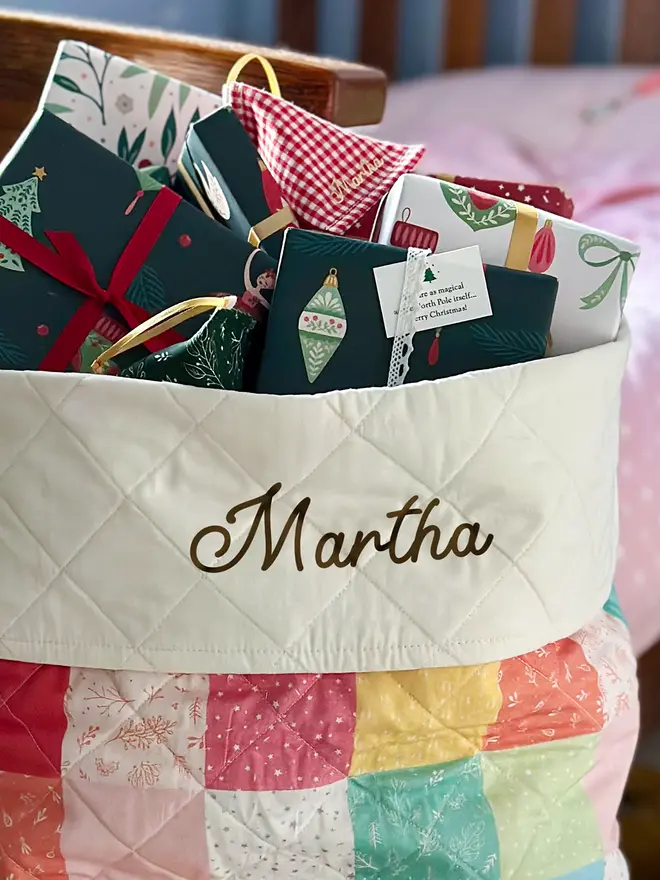 A tiny Christmas wish card is tucked into the ribbon on a wrapped gift at the top of a patchwork Christmas stocking.