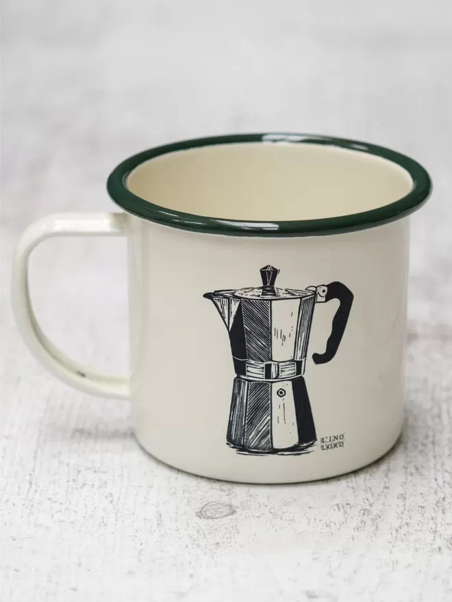 Picture of a Cream Enamel Mug with a Green Rim with a Moka Pot design etched onto it, taken from an original Lino Print