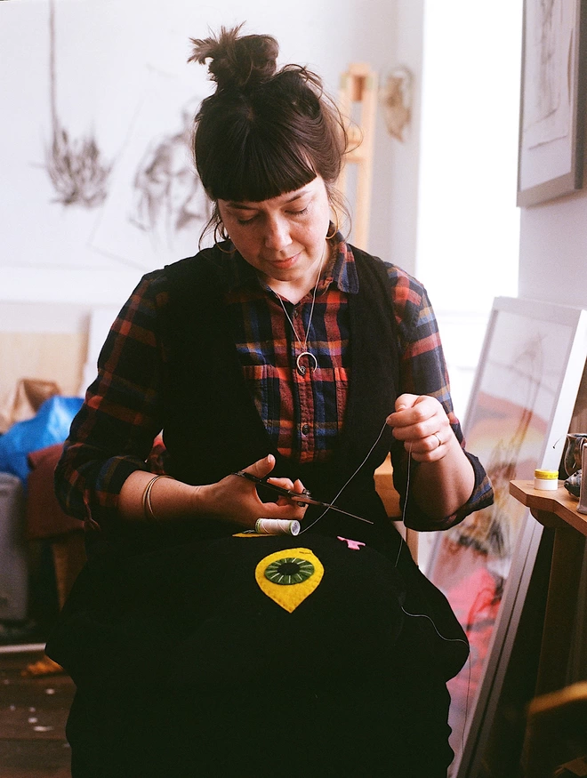 a white woman with dark hair sits sewinga cat cushion 