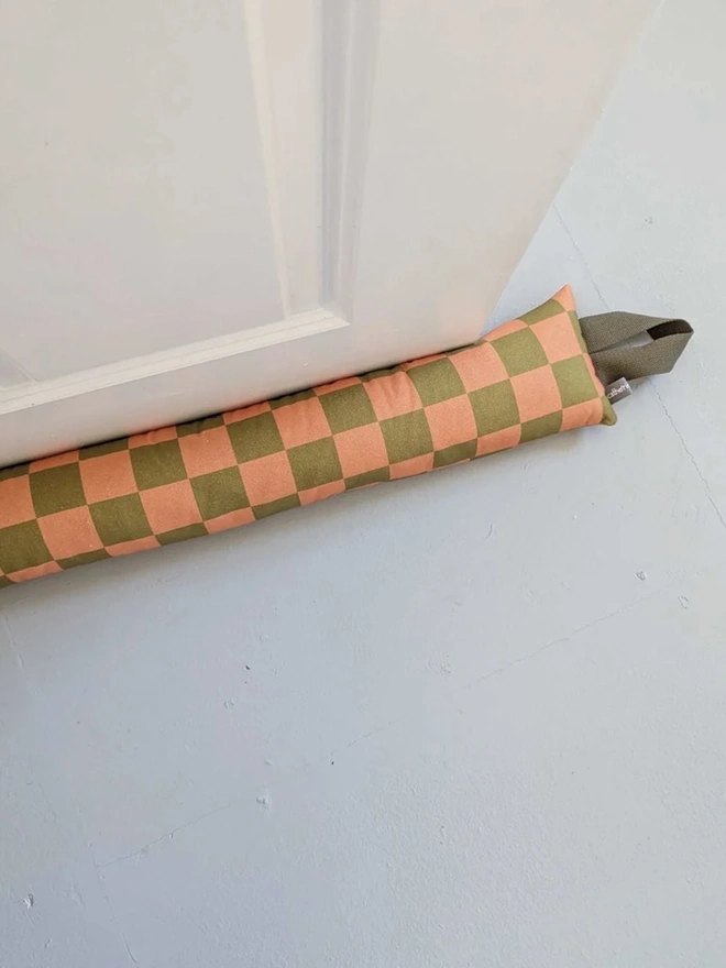 Draught Excluder, a colourful patterned draught excluder sitting on the floor by a white door. 
