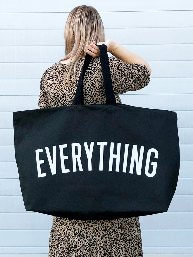 model holding an oversized black canvas tote bag with everything slogan