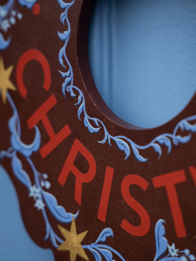 Depp Reddish Brown Hand painted Christmas Wreath with red lettering and gold leaf stars on a blue front door