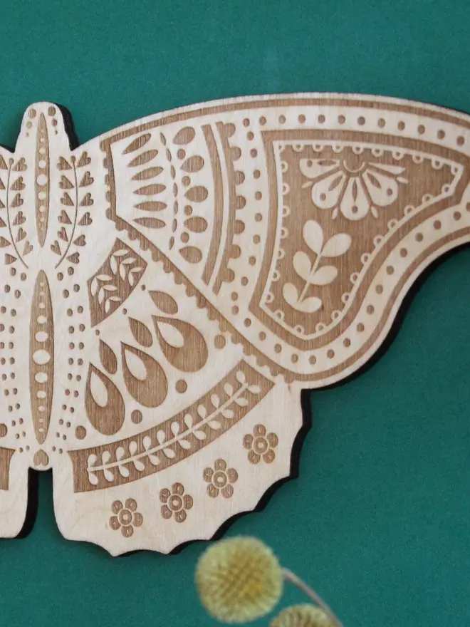 Wooden Folk Art Butterfly Hanging Decoration, wooden insect decoration hanging on a green wall. 
