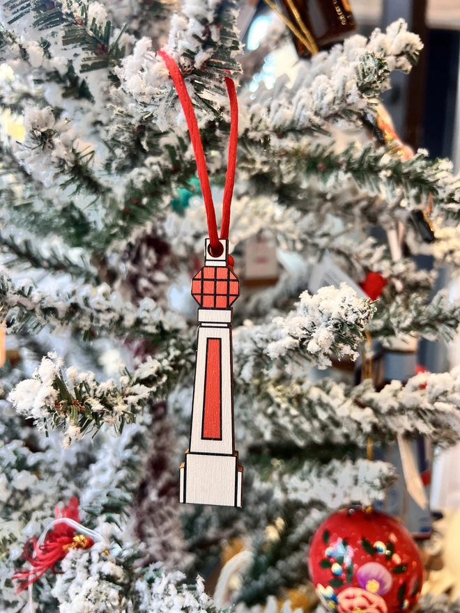 Small white and orange wooden tree decoration in the shape of Margate Lido sign. It is hanging by a red thread on a white fake Christmas Tree with other decorations. 