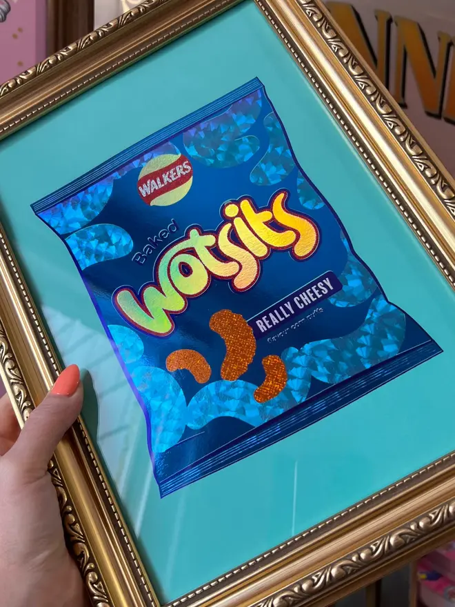 'Wotsits' ScreenPrint, a person holding a colourful wotsits screenprint in a frame. 